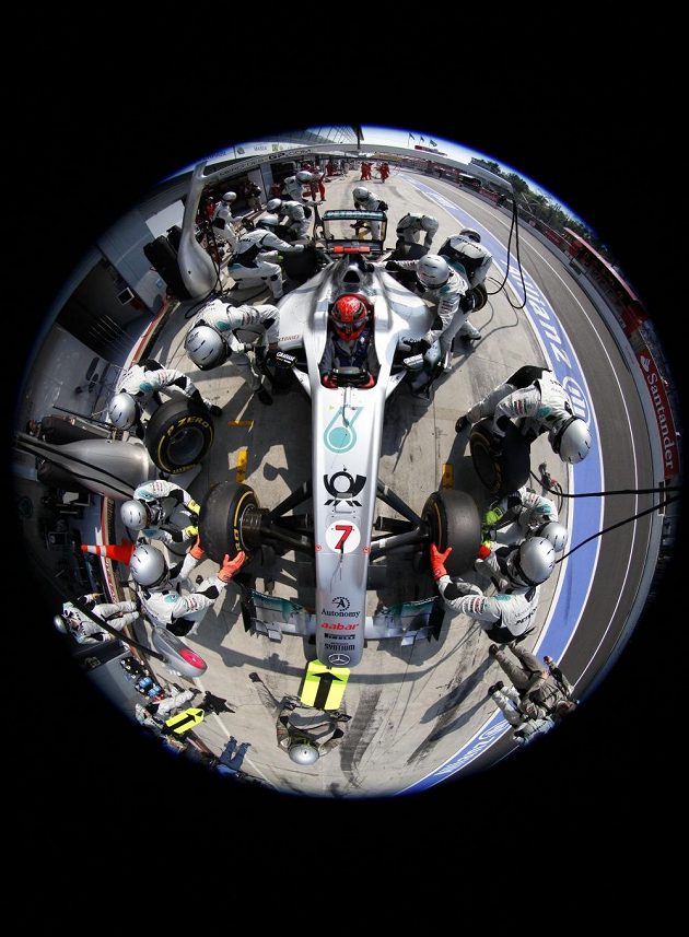 Pit stop. Fotoaparát upevněný na ramenu nad formulí, snímek "odpálený" na dálku.