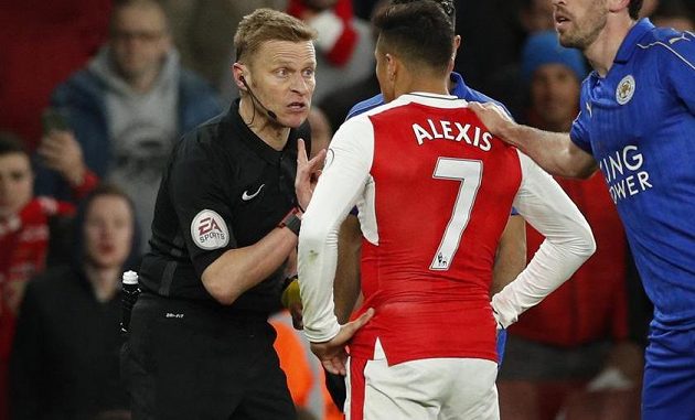 Rozhodčí Mike Jones vysvětluje útočníkovi Arsenalu, proč dostal žlutou kartu v duelu s Leicesterem. Alexis Sánchez se naopak snažil arbitra přesvědčit, že právě on byl obětí, když jej míč trefil do tváře.