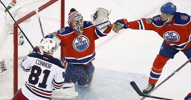 Adam Larsson (č. 6) z Edmontonu zkouší zachytit puk a pomoci tak brankáři Camu Talbotovi zastavit útočnou akci Kylea Connora z Winnipegu.