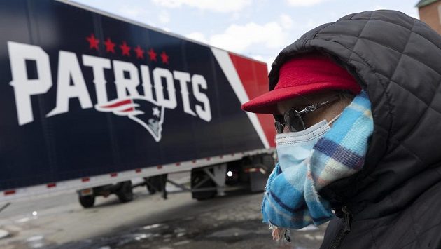 Žena s ochranou obliečeje sleduje náklaďák týmu New England Patriots. Žena s ochranou obliečeje sleduje náklaďák týmu New England Patriots.