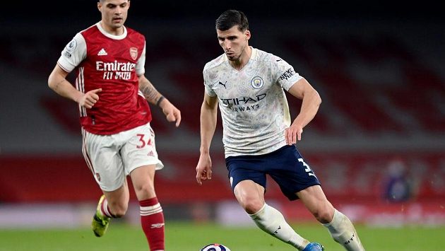 Ruben Dias z Manchesteru City v zápase Premier League s Arsenalem, vzadu jeho počínání sleduje Granit Xhaka. Ruben Dias z Manchesteru City v zápase Premier League s Arsenalem, vzadu jeho počínání sleduje Granit Xhaka.
