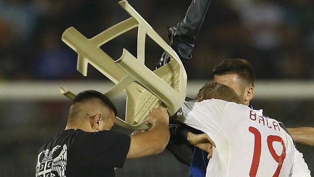 Srbský fanoušek se snaží zasáhnout židlí albánského útočníka Bekima Balaje (č. 19) během kvalifikačního utkání o postup na ME 2016 v Bělehradu. Srbský fanoušek se snaží zasáhnout židlí albánského útočníka Bekima Balaje (č. 19) během kvalifikačního utkání o postup na ME 2016 v Bělehradu.