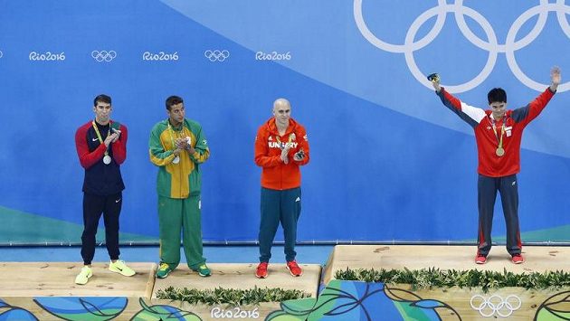 Zleva Michael Phelps, Chad Le Clos a Laszlo Cseh se tísní na stupni pro držitele stříbrné medaile. Vpravo vítěz Joseph Schooling. Zleva Michael Phelps, Chad Le Clos a Laszlo Cseh se tísní na stupni pro držitele stříbrné medaile. Vpravo vítěz Joseph Schooling.