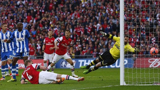 Per Mertesacker z Arsenalu vleže střílí gól v semifinále Anglického poháru proti Wiganu. Per Mertesacker z Arsenalu vleže střílí gól v semifinále Anglického poháru proti Wiganu.