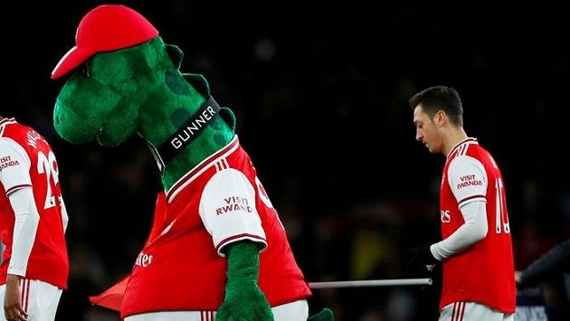 Německý fotbalista Mesut Özil kráčí za maskotem Arsenalu. Německý fotbalista Mesut Özil kráčí za maskotem Arsenalu.